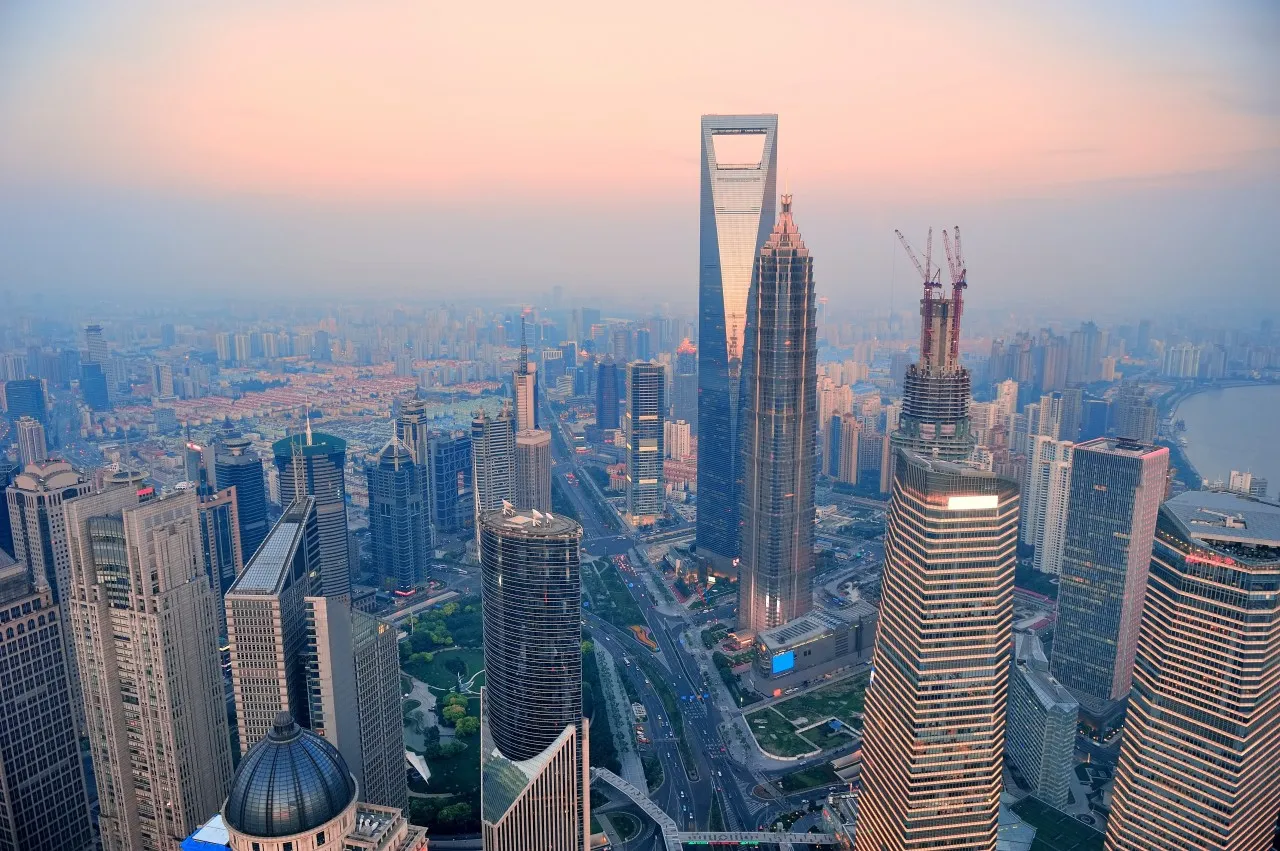 Panoramic view from above of Riyadh city with towering skyscrapers silhouetted against a pastel sky at dawn or dusk. City lights begin to twinkle in the twilight.